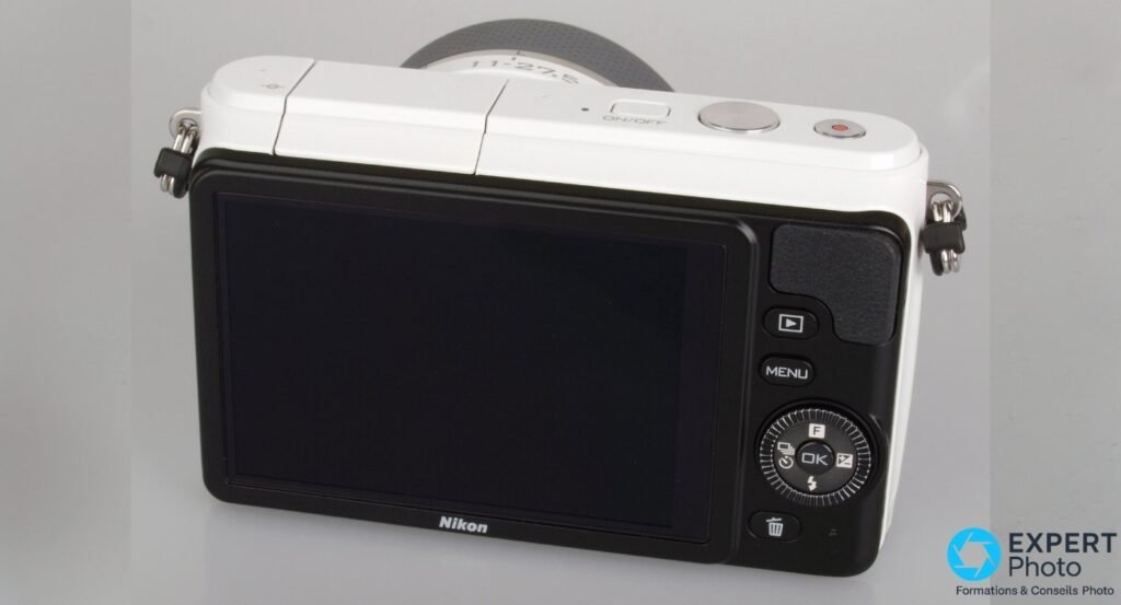 Dos du Nikon 1 S1 blanc, écran LCD fixe éteint, touches Play, MENU, corbeille et molette circulaire de navigation visibles.