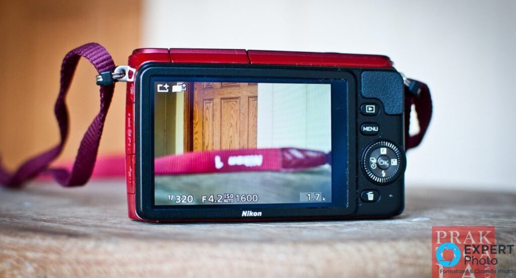 Dos du Nikon 1 S1 rouge, écran LCD affichant une scène intérieure en live view avec 1/320 f/4.2 ISO 1600, molette visible.