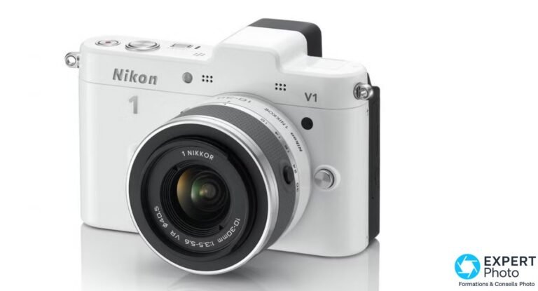 Nikon 1 V1 blanc avec objectif 1 NIKKOR VR 10-30mm f/3.5-5.6 monté, vu de trois quarts face, fond studio