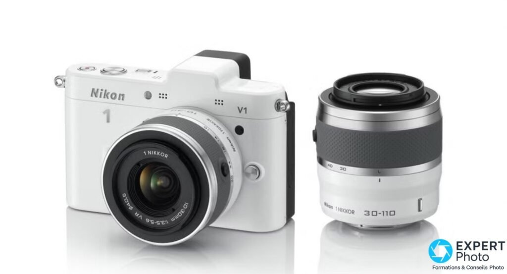 Nikon 1 V1 blanc avec 1 NIKKOR VR 10-30mm monté et 1 NIKKOR VR 30-110mm posé à côté, fond studio clair