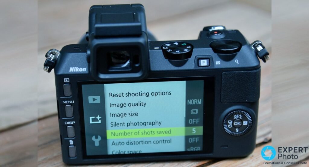 Nikon 1 V2 noir vu de dos sur bois, écran allumé sur menu shooting options, viseur EVF, boutons MENU et DISP, molette AE-L 