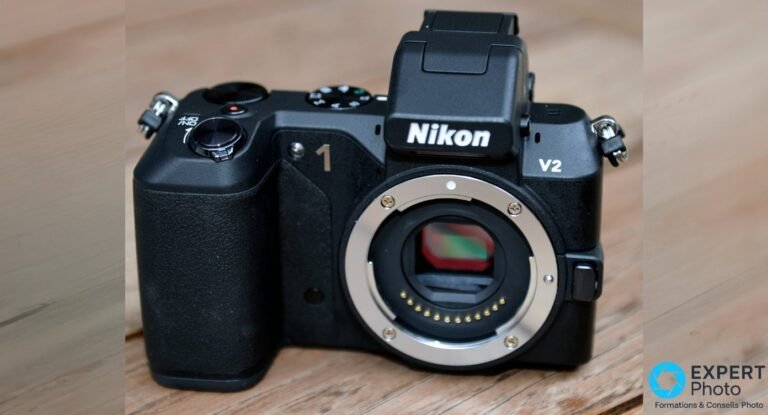 Nikon 1 V2 noir boîtier nu posé sur bois, marquage Nikon 1 V2, monture Nikon 1 ouverte avec capteur CX et contacts dorés