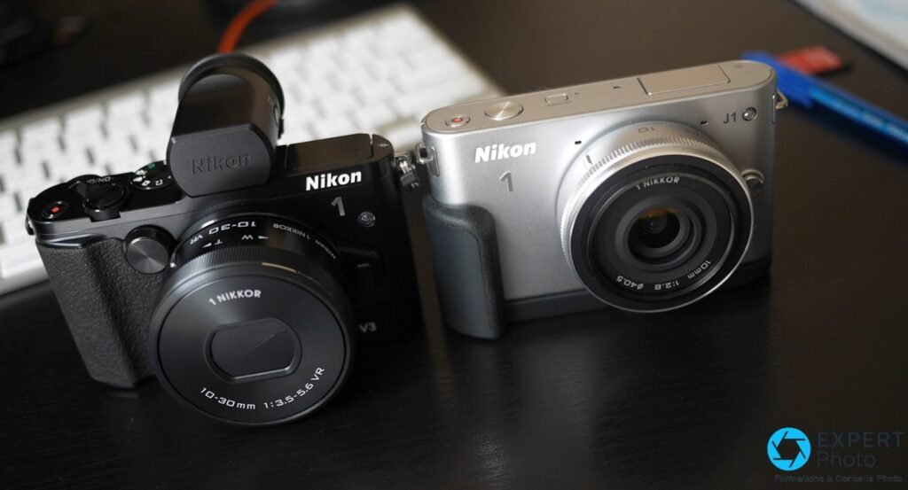 Nikon 1 V3 noir avec viseur DF-N1000 et 10-30 mm à gauche, Nikon 1 J1 argenté avec 1 NIKKOR 10 mm f/2.8 à droite