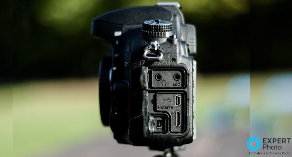 Gros plan prises ouvertes Nikon D600 : prise casque, MIC, port USB micro, HDMI mini et GPS en bas, fond bokeh sombre.