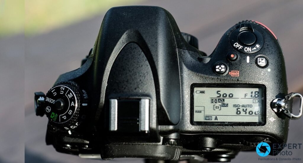 Nikon D600 vu du dessus, molette de modes P S A M U1 U2 SCENE, LCD affichant 1/500 f/1.8 ISO-AUTO 6400 RAW.