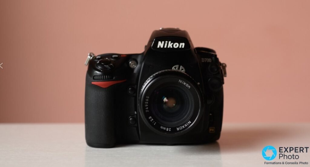 Nikon D700 vu de dos sur table en bois, viseur pentaprisme, écran LCD éteint, boutons MENU OK, slot CF, accessoires rouges