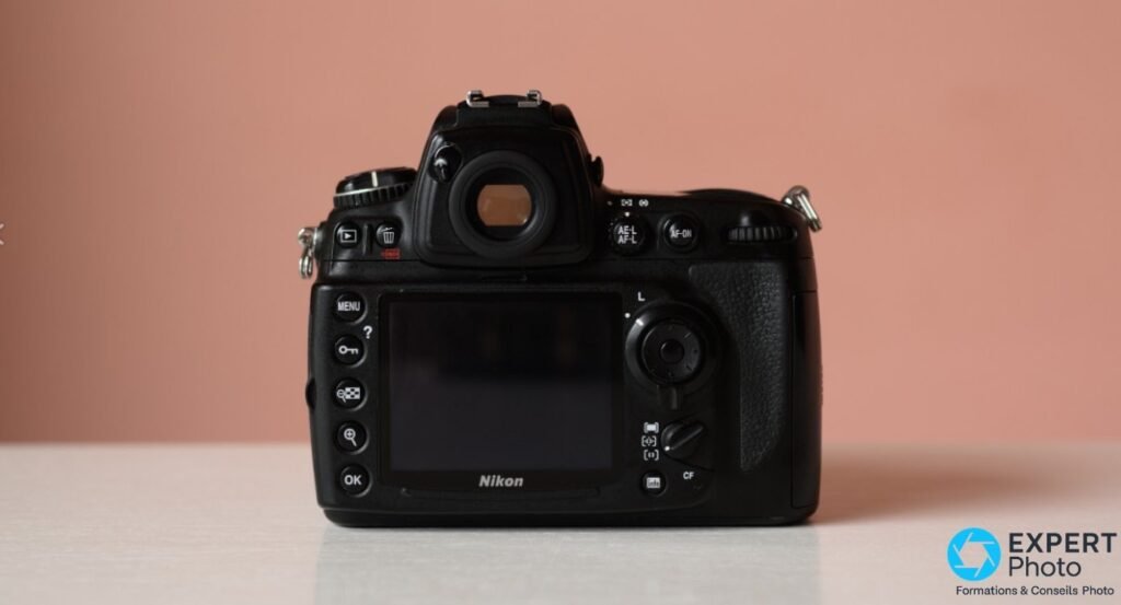 Nikon D700 photographié de face sur fond rose, objectif Nikkor 28mm f/2.8 monté, badge FX et logo Nikon D700 visibles