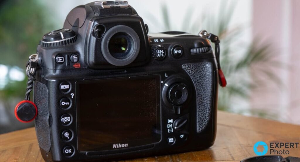 Nikon D700 posé sur table en bois, vue trois quarts avant gauche, objectif AF Nikkor 85mm f/1.8D, lanière rouge