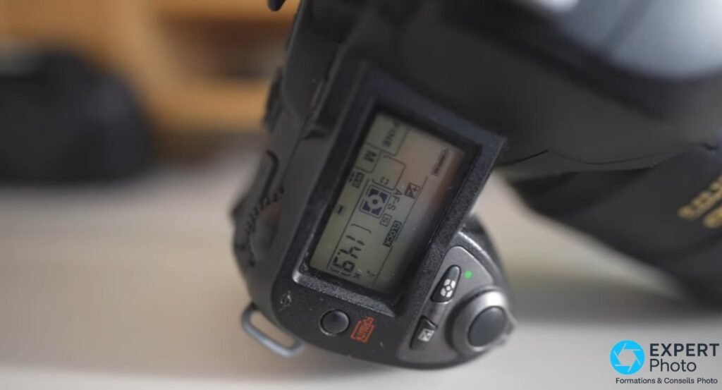 Nikon D70s gros plan sur le panneau LCD inférieur, affichant les réglages AF-S et informations de capture, objectif visible.