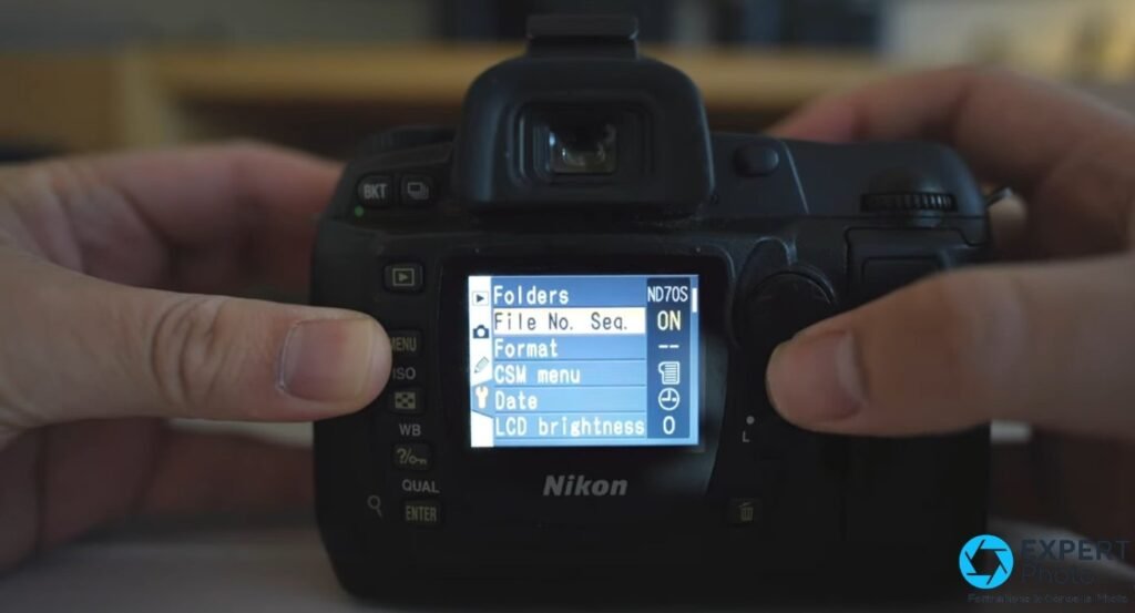 Nikon D70s tenu à deux mains, écran LCD affichant le menu Folders, File No., Format, CSM menu, Date, LCD brightness.