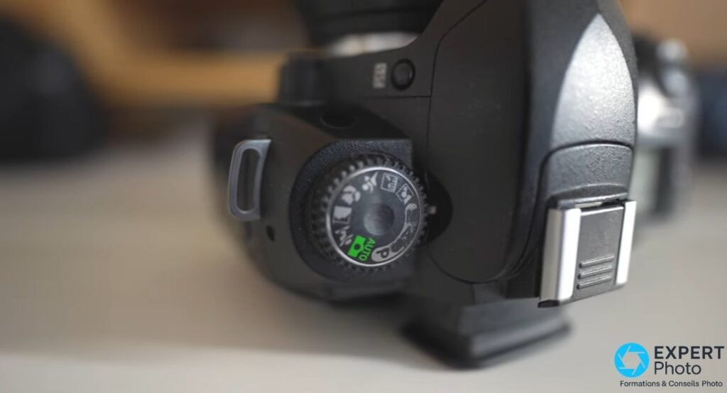 Nikon D70s gros plan sur la molette de modes, position AUTO sélectionnée en vert, sabot flash chromé visible à droite.