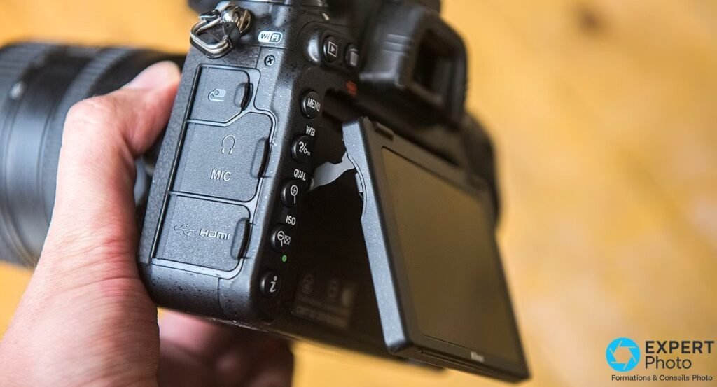 Nikon D750 tenu en main, face latérale gauche avec ports MIC, HDMI et casque, boutons MENU WB QUAL ISO et écran inclinable 