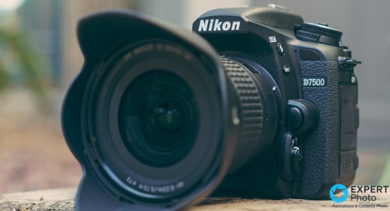 Nikon D7500 posé en extérieur face avant avec objectif grand-angle et pare-soleil pétale, logo D7500 visible, bokeh naturel