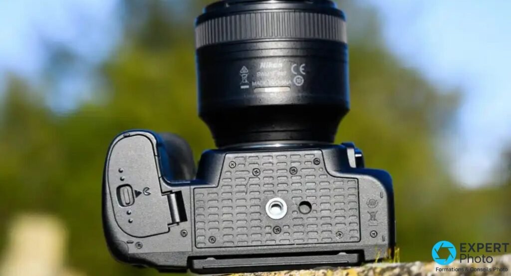 Nikon D780 vue de dessous en extérieur, pas de vis trépied central et trappe batterie visibles, objectif Nikon monté