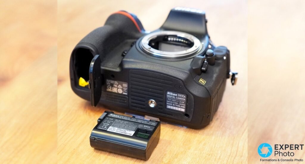 Nikon D810A vu de dessous, compartiment batterie ouvert et batterie EN-EL15 posée à côté, monture F visible 