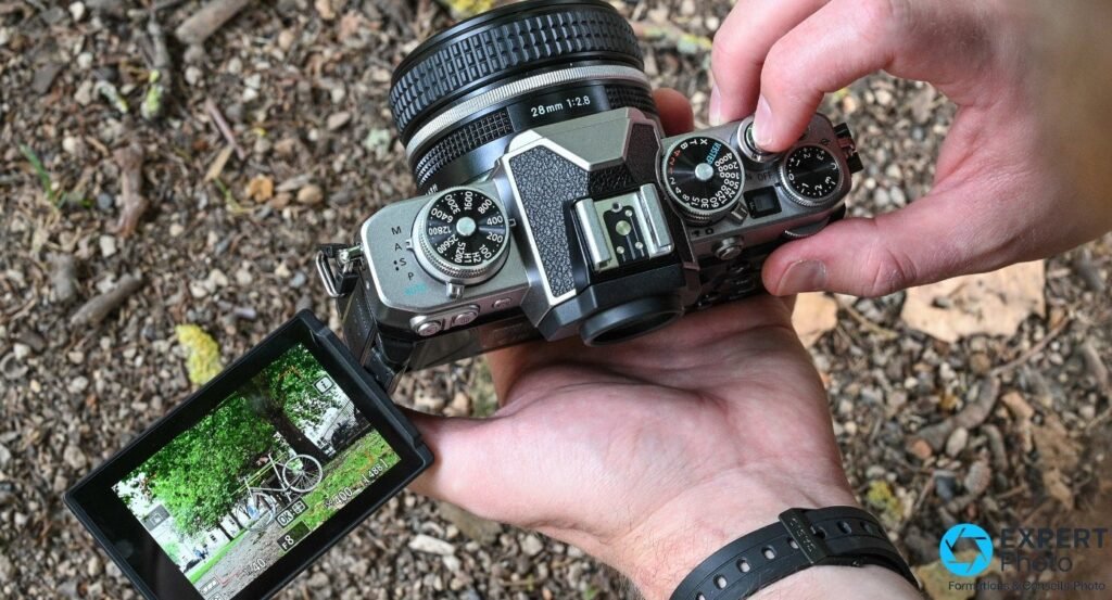 Nikon Z fc tenu à deux mains en extérieur, vue plongée, écran tactile sur rotule déployé et objectif 28 mm f/2.8.