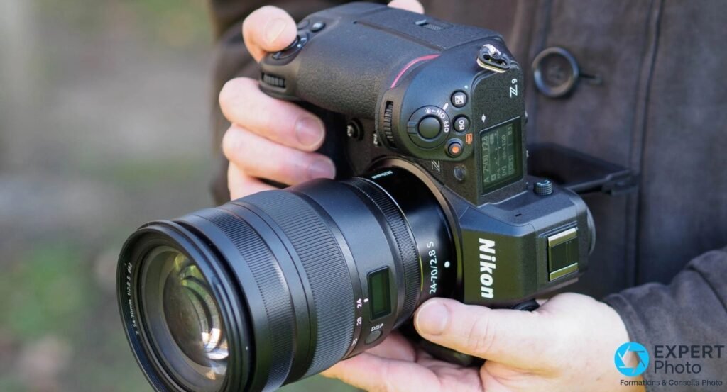 Nikon Z9 tenu en vue trois quarts avec objectif 24-70 f/2.8 S, écran LCD supérieur visible, fond extérieur flou 