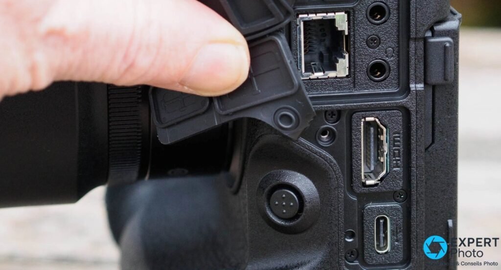 Gros plan sur les ports du Nikon Z9 : RJ45 Ethernet, HDMI pleine grandeur et USB-C, cache caoutchouc ouvert par une main