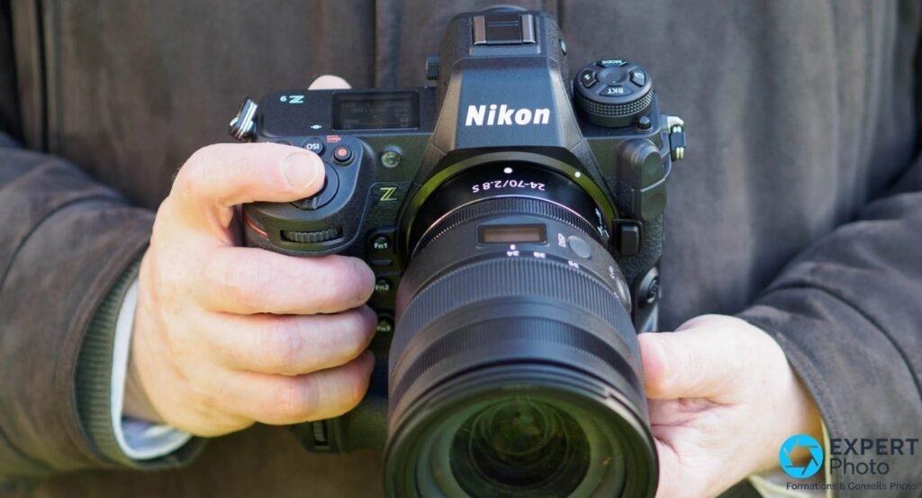 Nikon Z9 tenu à deux mains en gros plan face avant, objectif Nikkor Z 24-70 f/2.8 S monté, photographe en veste visible