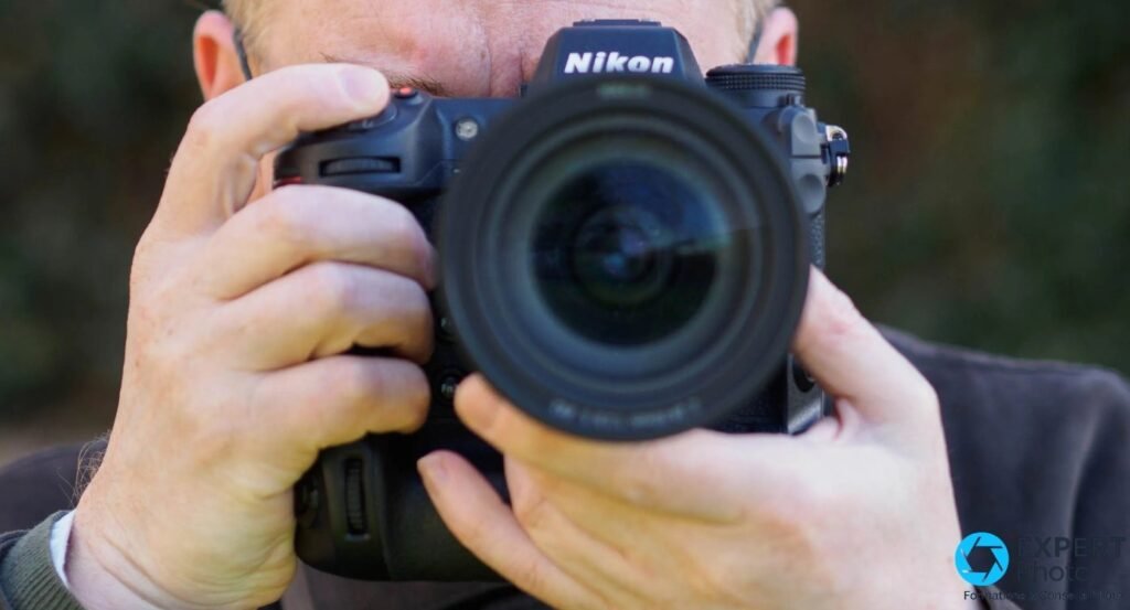 Photographe utilisant un Nikon Z9 au viseur avec objectif zoom monté, vue de face, extérieur en contre-plongée légère