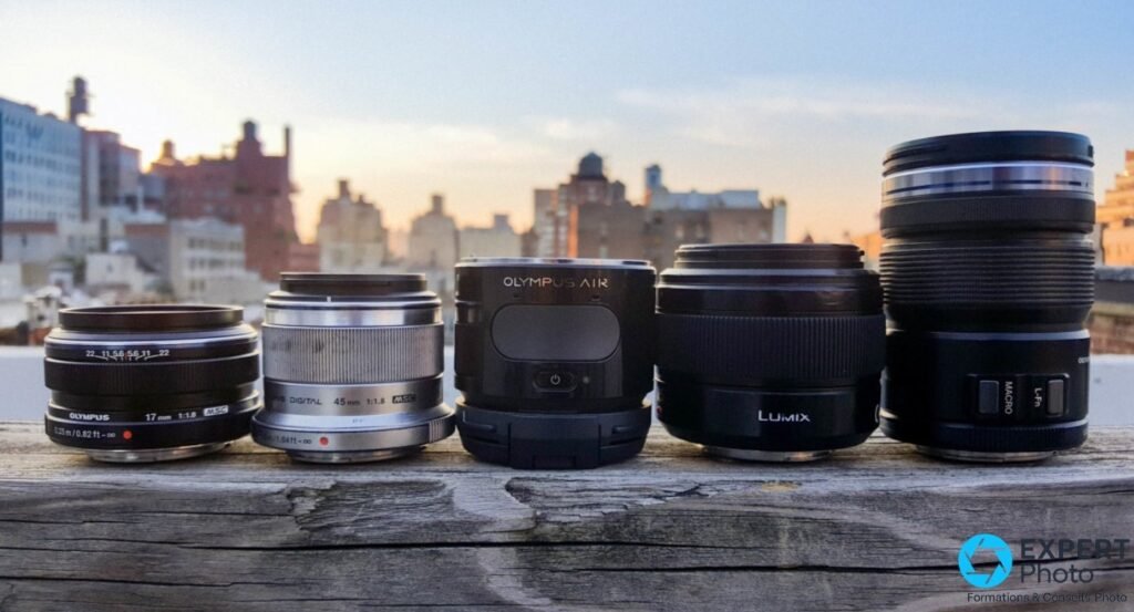 Olympus AIR A01 aligné à côté de cinq objectifs Micro Four Thirds Olympus et Panasonic LUMIX sur traverse bois, skyline 