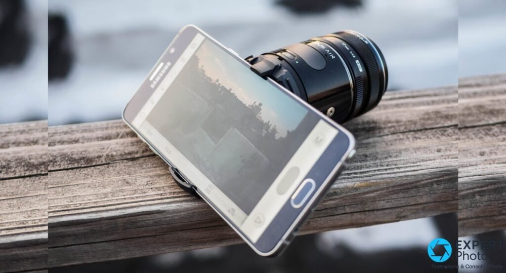 Olympus AIR A01 avec objectif Olympus monté et smartphone Samsung incliné affichant le cadrage, vue trois-quarts