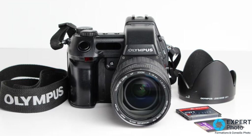 Olympus E-10 de face avec objectif 9-36 mm f/2-2.4, sangle OLYMPUS, pare-soleil LH-1 et cartes CompactFlash SanDisk.