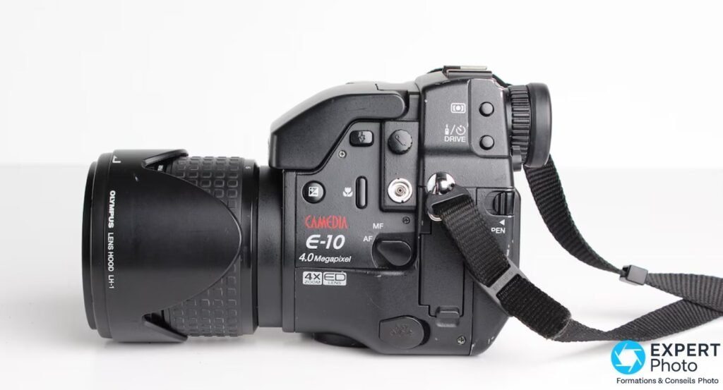 Profil gauche de l'Olympus E-10, marquage CAMEDIA E-10 4.0 Megapixel visible, pare-soleil LH-1 et commutateur MF/AF. 