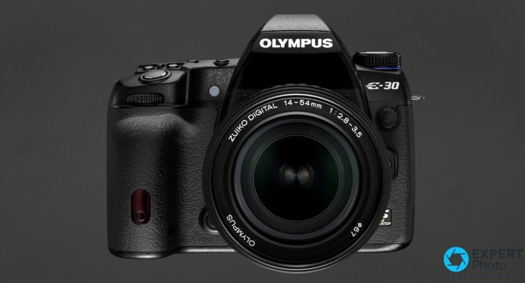 Olympus E-30 vu de face avec objectif Zuiko Digital 14-54mm f/2.8-3.5, voyant AF rouge visible sur le grip.
