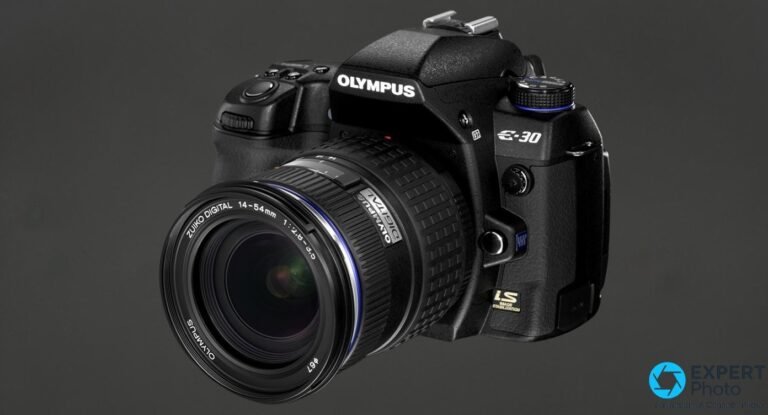 Olympus E-30 en vue 3/4 avant avec objectif Zuiko Digital 14-54mm f/2.8-3.5, badge IS visible sur le boîtier.