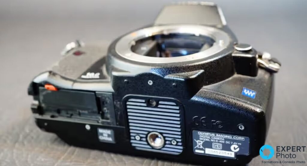 Olympus E-400 vu du dessous, trappe batterie ouverte, plaque signalétique avec modèle E-400 et numéro de série. 