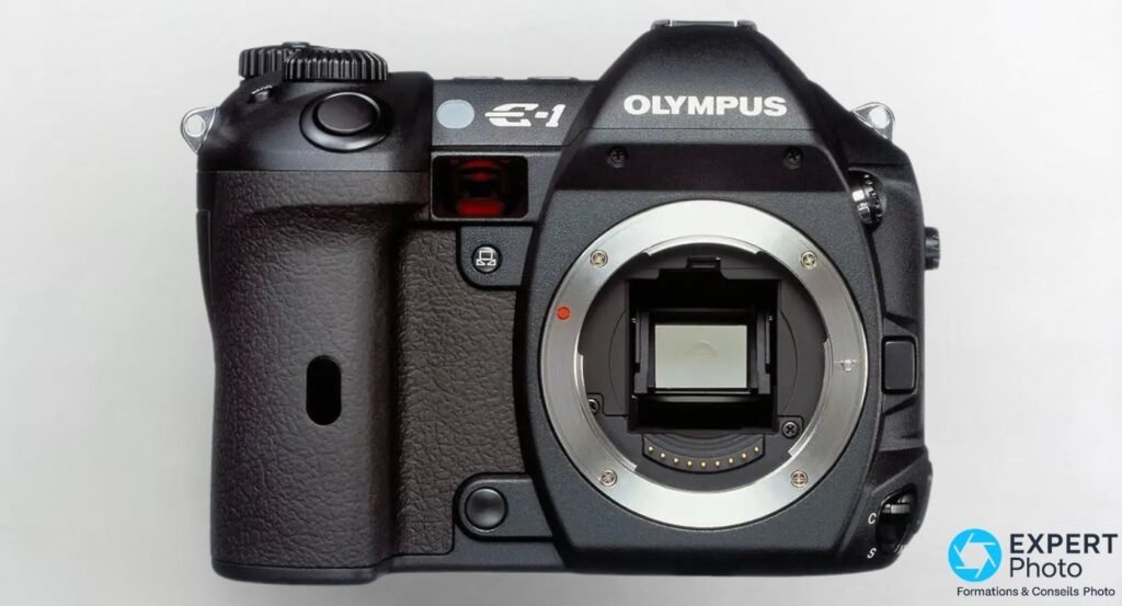  Olympus E-1 boîtier reflex numérique noir, vue de face sans objectif, monture Four Thirds exposée sur fond clair. 
