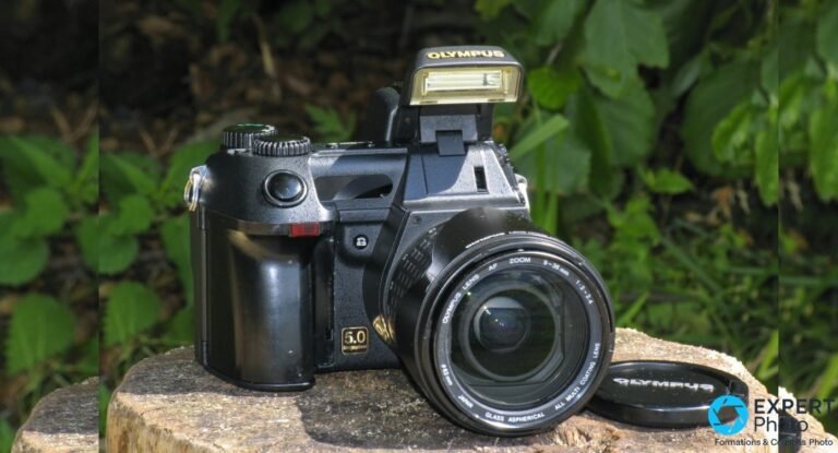 Olympus E-20 en vue de face trois quarts, flash intégré relevé, objectif 9-36 mm f/2-2,4 et bouchon Olympus posé