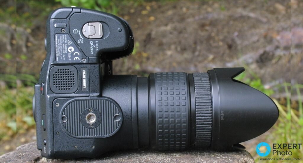 
Olympus E-20 de profil, sous-plaque visible avec étiquette constructeur, numéro de série et filetage trépied