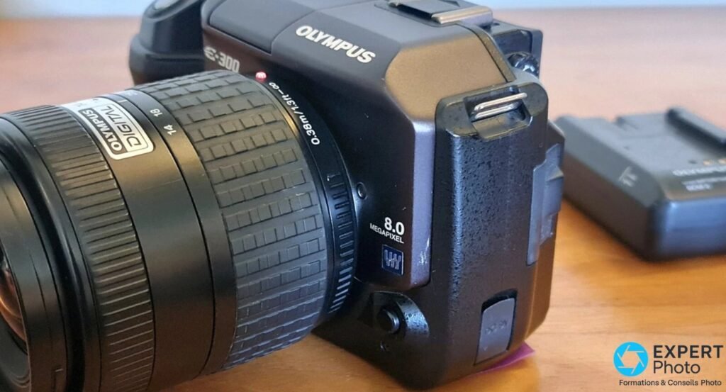 Profil droit du boîtier Olympus E-300 avec logos OLYMPUS, E-300 et marquage 8.0 MEGAPIXEL sur le flanc.