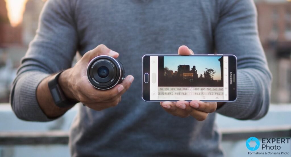 Objectif Olympus M.Zuiko 17mm f/1.8 dans une main et smartphone Samsung affichant l'interface de pilotage photo dans l'autre 