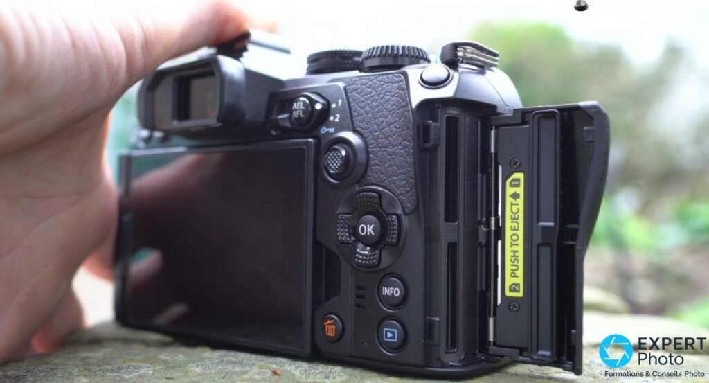 Double slot SD de l'Olympus OM-D E-M1 Mark III avec trappe ouverte, étiquette jaune PUSH TO EJECT sur le slot 2.