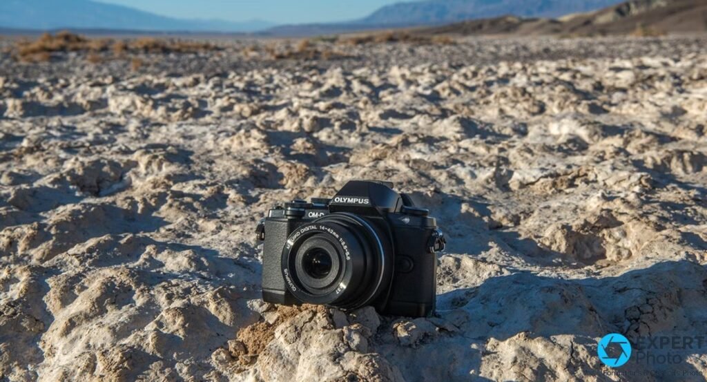 Boîtier Olympus OM-D E-M10 noir avec zoom 14-42 mm posé sur un sol rocheux, paysage désertique au fond