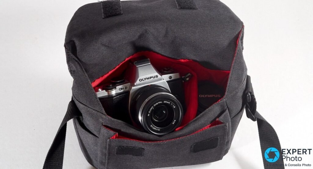 Olympus OM-D E-M5 argent avec 25 mm f/1.8 rangé dans un sac photo toile gris foncé à intérieur rouge.