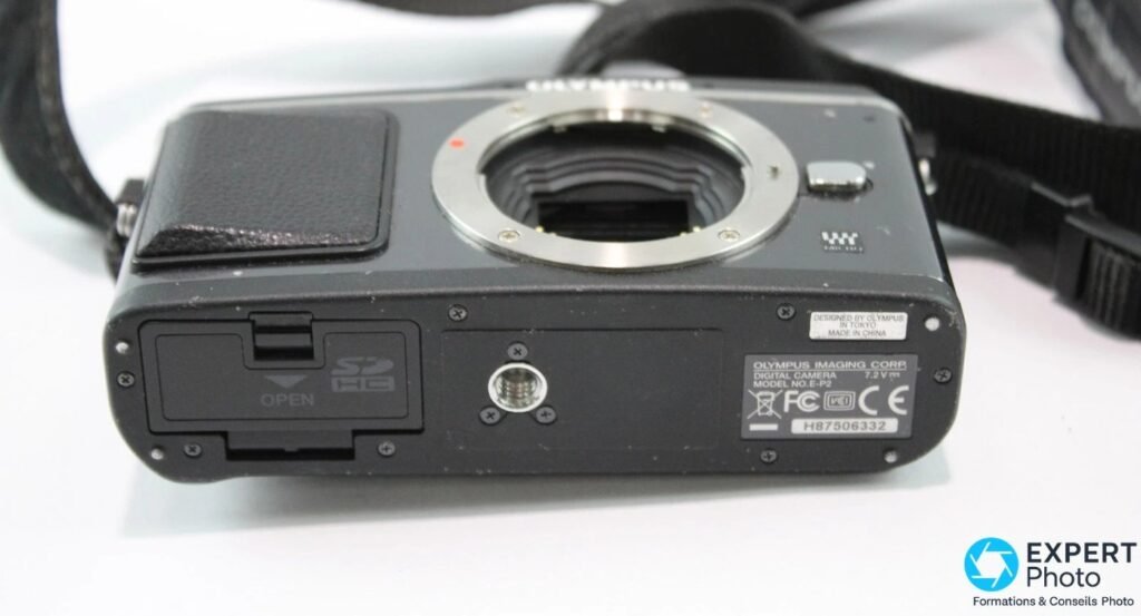 Dessous de l'Olympus PEN E-P2 avec plaque constructeur « Digital Camera Model E-P2 », trappe carte SDHC et filetage trépied. 