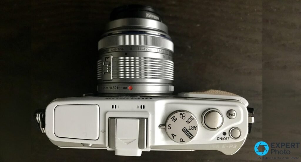 Vue de dessus de l'Olympus PEN E-P3 blanc avec objectif M.Zuiko 14-42 mm monté, molette de mode et bouton Fn2 visibles