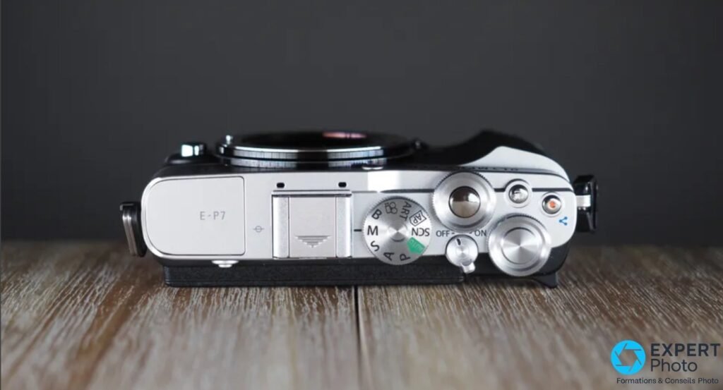 Olympus PEN E-P7 vu du dessus sans objectif, gravure E-P7 sur le capot flash, molette PASM et déclencheur.