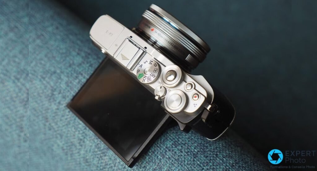 Olympus PEN E-P7 vu du dessus en plongée, objectif M.Zuiko 14-42 mm EZ monté, écran inclinable rabattu.