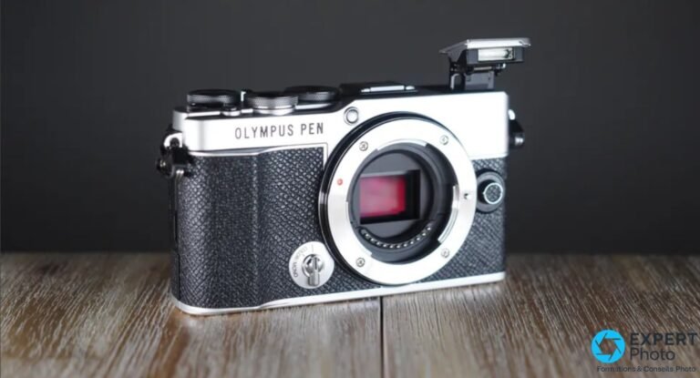 Olympus PEN E-P7 argent et noir vu de face sans objectif, flash pop-up déployé, monture Micro 4/3 exposée.