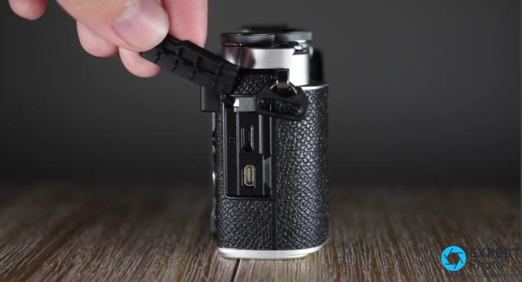 Main ouvrant le cache caoutchouc du côté gauche de l'Olympus PEN E-P7, ports micro-HDMI et USB 2.0 visibles.