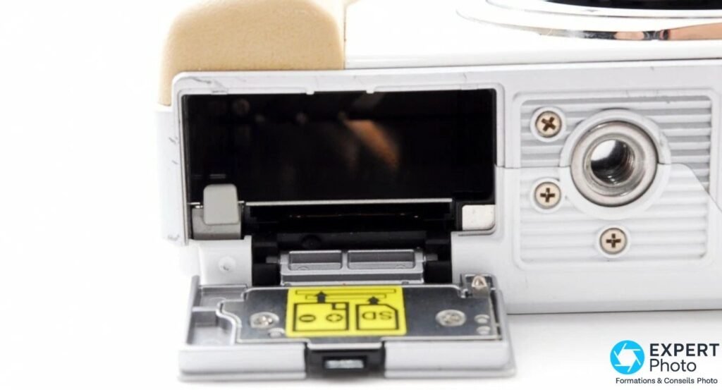 Compartiment batterie et carte SDHC de l'Olympus PEN E-PL1 ouvert, avec sticker d'orientation jaune à l'intérieur. 