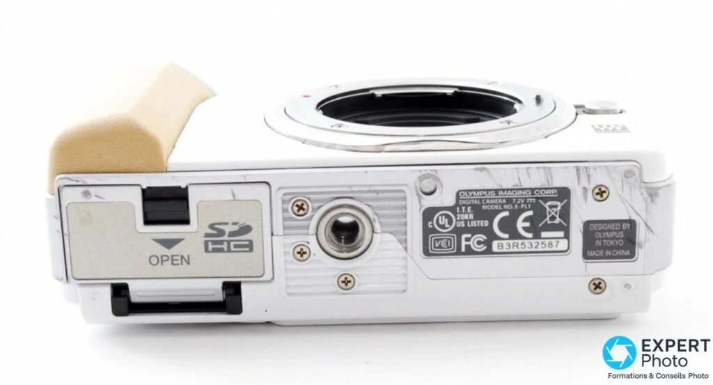 Dessous de l'Olympus PEN E-PL1 : plaque « MODEL NO. E-PL1 », numéro de série, socle trépied et porte SDHC marquée OPEN. 