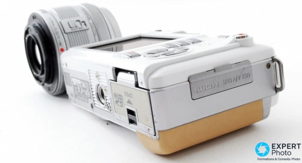 Olympus PEN E-PL1 blanc équipé d'un zoom silver Micro 4/3, vu de 3/4 arrière avec trappe USB/AV/HDMI visible.