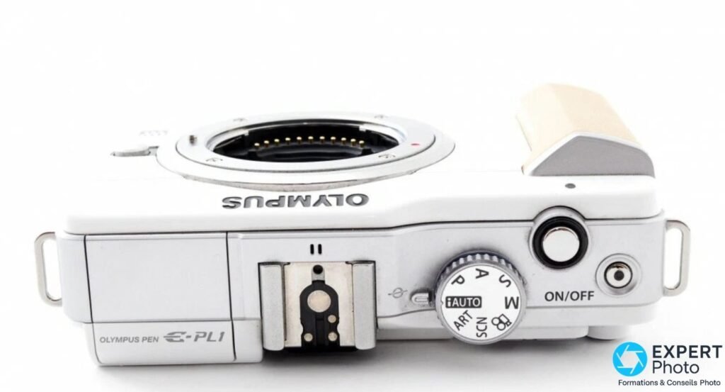Dessus de l'Olympus PEN E-PL1 : mode dial iAUTO/P/A/S/M/ART/SCN, hot shoe avec port AP2 et gravure OLYMPUS PEN E-PL1.