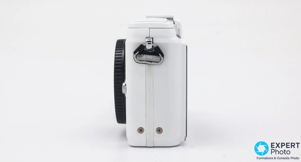 Olympus PEN E-PL2 blanc vu de profil gauche, anneau de sangle avec mousqueton et flash rabattu